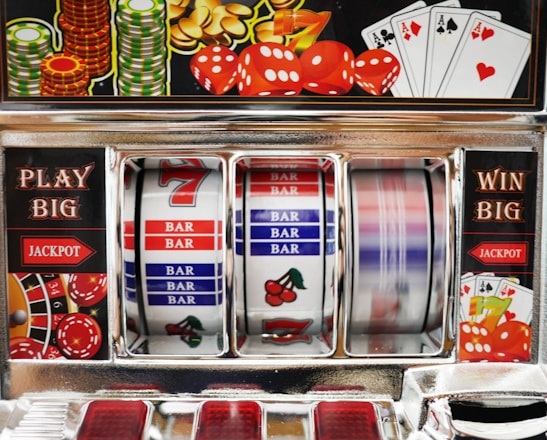 A close-up view of a slot machine with vibrant colors and various gambling symbols such as dice, coins, and playing cards. The reels display a combination of symbols, including bars, cherries, and the number seven. The chrome exterior and colorful details convey the theme of casino and gambling.