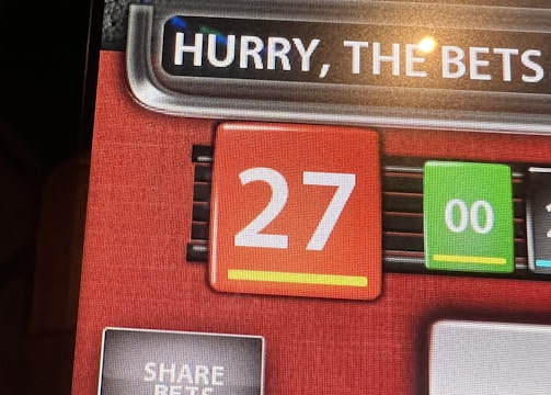 A digital display screen showing a casino betting interface, with text prompting to hurry bets and a highlighted number 27 in red. There are options for betting amounts and a 'share bets' button.