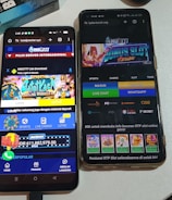 Two smartphones are displayed on a white surface, both showing gambling websites with colorful graphics, text, and various options for logging in and accessing games. The screens are bright and filled with promotional content related to casino and slot games.