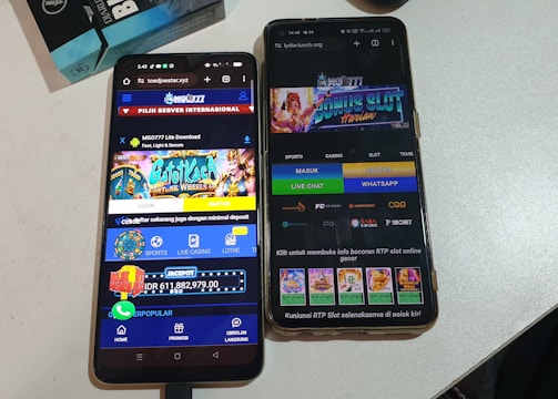 Two smartphones are displayed on a white surface, both showing gambling websites with colorful graphics, text, and various options for logging in and accessing games. The screens are bright and filled with promotional content related to casino and slot games.